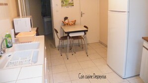 A small kitchen with a white refrigerator, a dining table with chairs, and a microwave. There is a door leading to another room and a poster on the wall. - Quiet, restful gîte in town. Everything is less than 500m away on foot! (Beaumont-De-Lomagne)