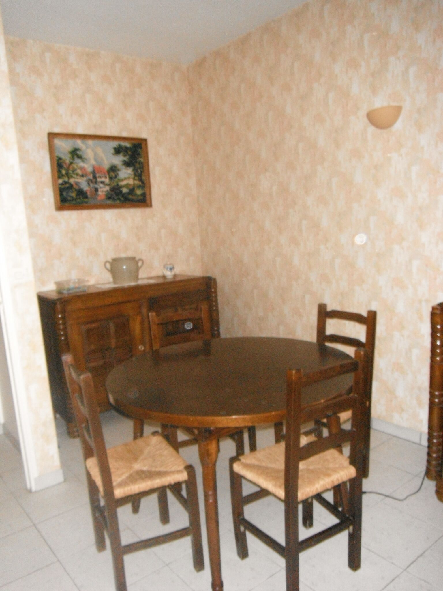 Un comedor con una mesa redonda de madera y seis sillas, un aparador de madera y una lámpara fijada a la pared.