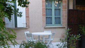 A patio area with a white table and chairs, surrounded by potted plants and a small decorative item. - Quiet, restful gîte in town. Everything is less than 500m away on foot! (Beaumont-De-Lomagne)