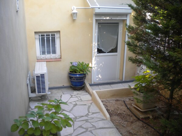 A small, enclosed outdoor area with a stone floor, a potted plant, and a white door. - Cosy, well-kept studio ideal for holidaymakers (Martigues)