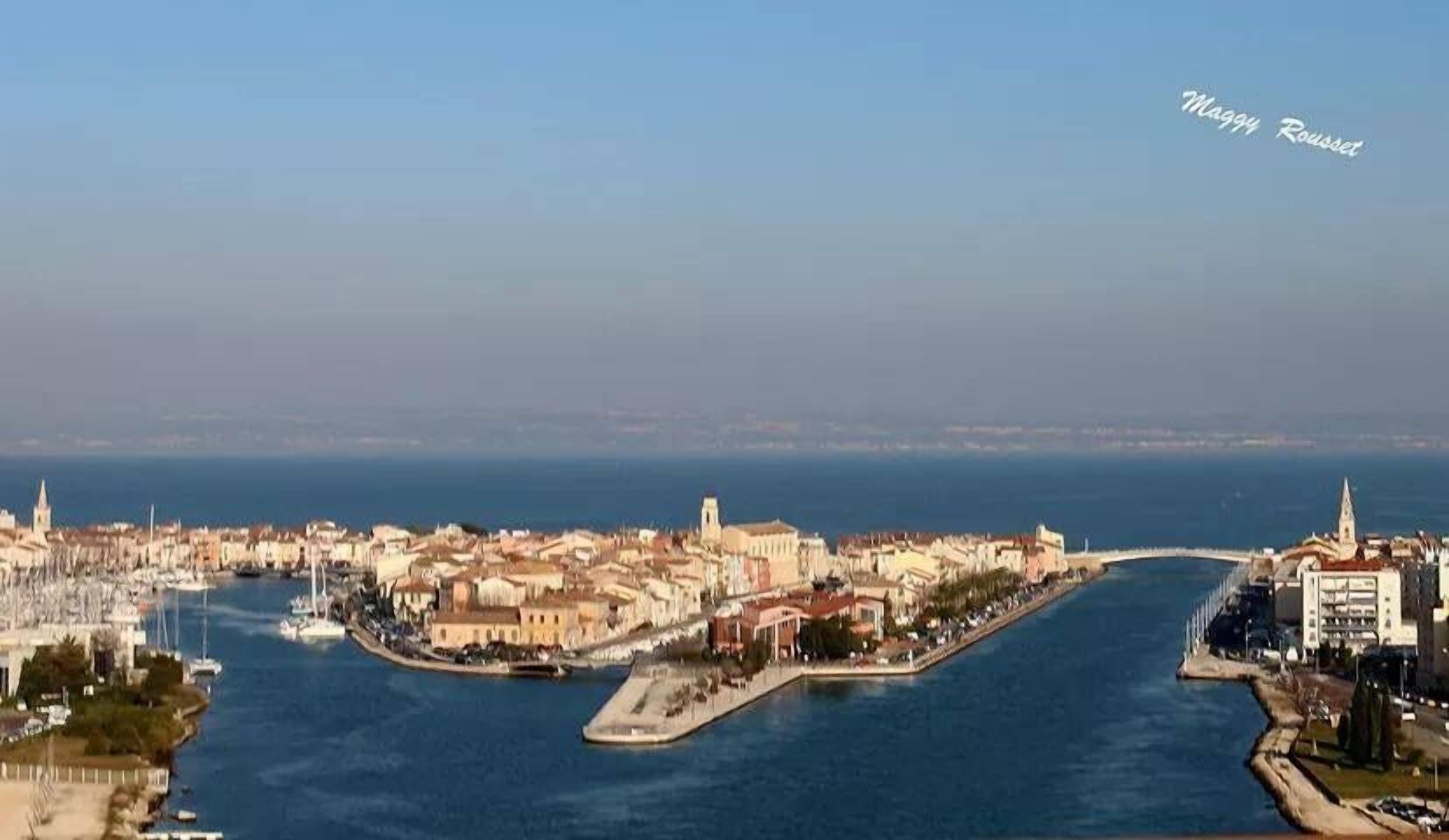 A coastal cityscape with a prominent peninsula featuring historic buildings and a marina.