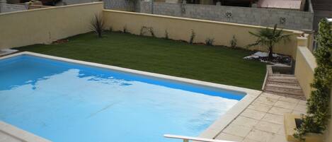 A swimming pool with a clear blue water surface, surrounded by a well-maintained lawn and a stone wall.