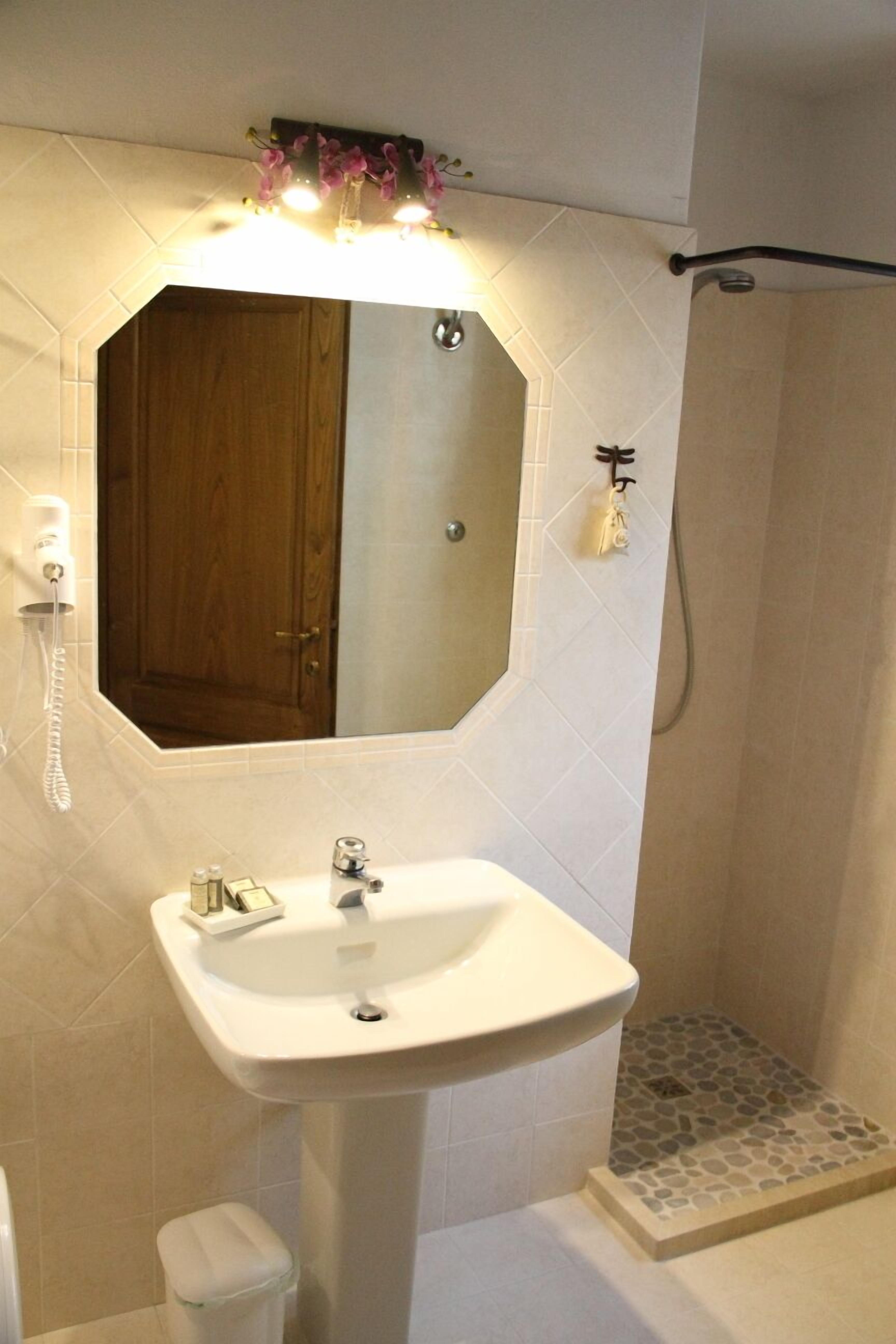 Un bagno con un lavandino bianco, uno specchio, una doccia e un water.