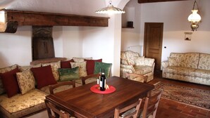 A cozy living room with a wooden dining table, floral sofas, and a red rug.