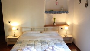 A hotel room with a large bed, two bedside tables with lamps, a small shelf with decorative items, and a wall-mounted shelf above the bed.