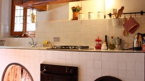 A kitchen with white tiled walls, wooden beams, a stove, oven, and a window with curtains.