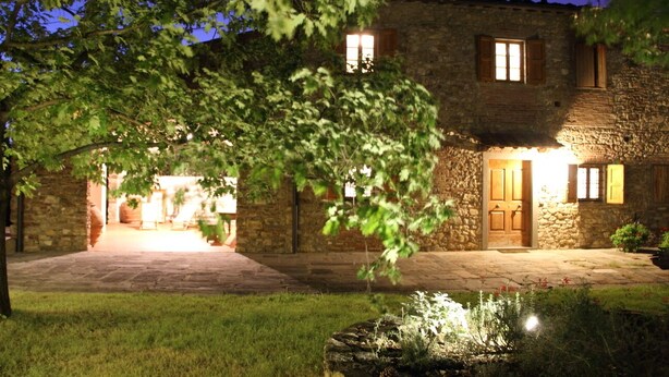 A stone building with a well-lit entrance, a paved driveway, and a small water feature in the foreground.