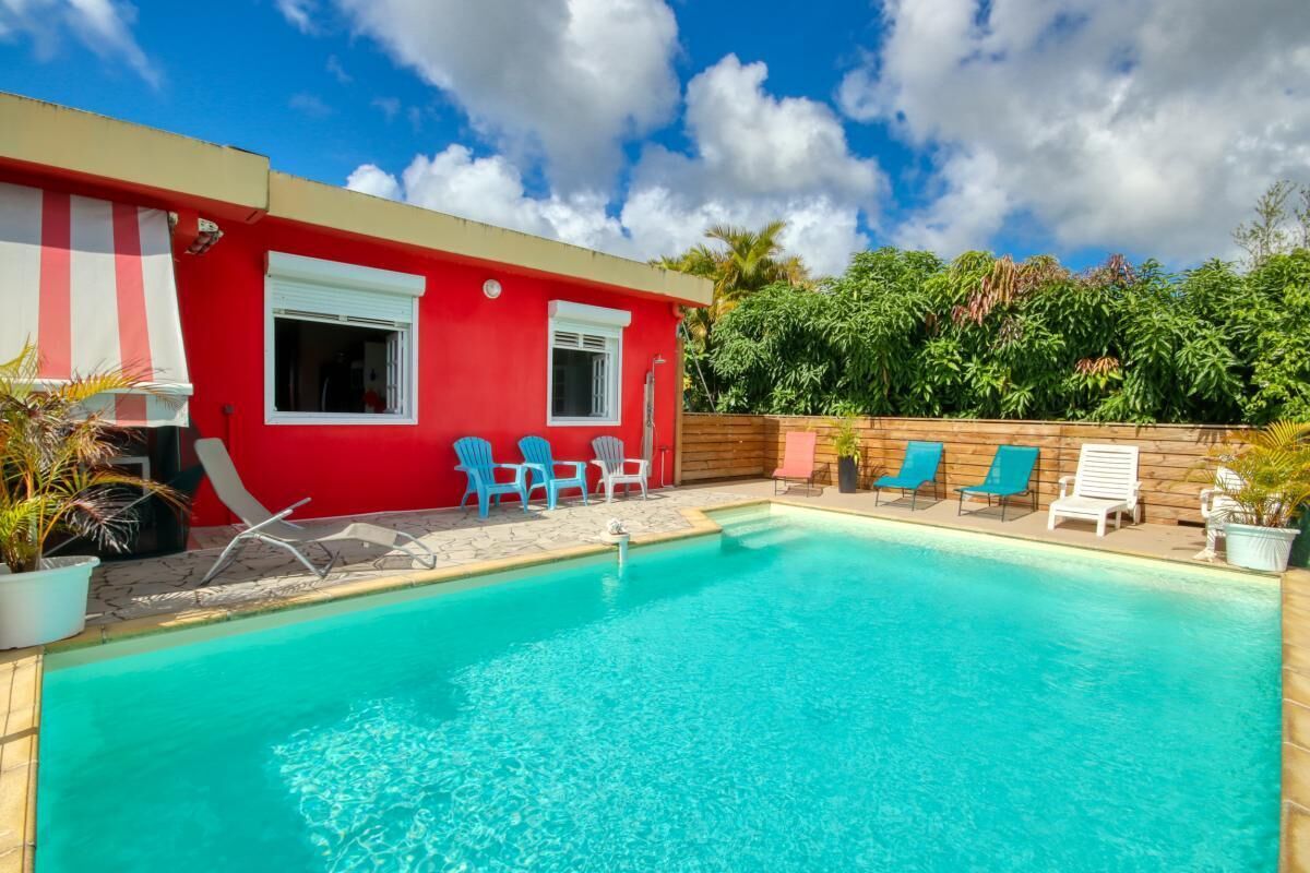 A red building with a pool, blue chairs, and a wooden fence.