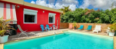 A red building with a pool, blue chairs, and a wooden fence.