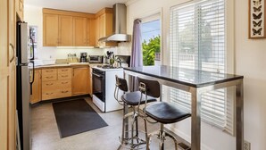 A compact kitchen with wooden cabinets, a stainless steel range hood, a gas stove, and a bar stool. - 2 Bedroom Condo Only 1 Block to UCB (Berkeley)