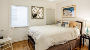 A bedroom with a bed, a chair, a window, a wall art piece, and a lamp. - 2 Bedroom Condo Only 1 Block to UCB (Berkeley)