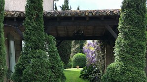 A gravel pathway leading to a wooden pergola with a hanging light fixture, surrounded by neatly trimmed evergreen shrubs and a small, manicured lawn. - Maison de Maître, manor house style, on the banks of the Lot, countryside, heated swimming pool, tennis court, sauna (Casseneuil)