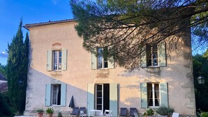 A two-story house with a stone facade, green shutters, and a patio with outdoor furniture. - Maison de Maître, manor house style, on the banks of the Lot, countryside, heated swimming pool, tennis court, sauna (Casseneuil)