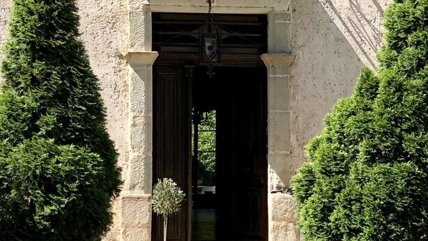 A stone building with a dark wooden door, a small potted plant, and trimmed bushes on either side. - Maison de Maître, manor house style, on the banks of the Lot, countryside, heated swimming pool, tennis court, sauna (Casseneuil)