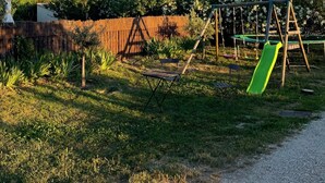 A playground with a slide and swings, surrounded by a fence and greenery. - charming house in Provence (Beaumes-De-Venise)