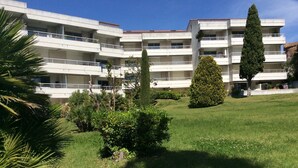 A multi-story building with balconies, surrounded by well-maintained lawns and various trees.