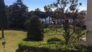 A well-maintained garden with various trees and shrubs, a sign indicating a private area, and a view of a body of water in the background.