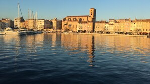 A waterfront cityscape with historic buildings, a prominent church with a bell tower, and boats docked along the quay.
