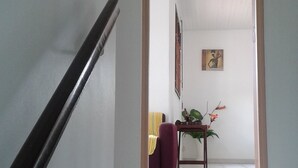 Een trap die leidt naar een kamer met een betegelde vloer, een ingelijst beeld aan de muur en een klein tafeltje met een plant.