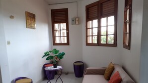 Een ruime, goed verlichte kamer met een bank, een klein tafeltje met een plant en een paarse stoel.