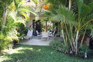 A patio with a table and chairs, surrounded by lush greenery and a palm tree. - 1BR/2BA Maui Kamaole/Wailea Border. K Cluster @ Tropical Pool! (Kihei)
