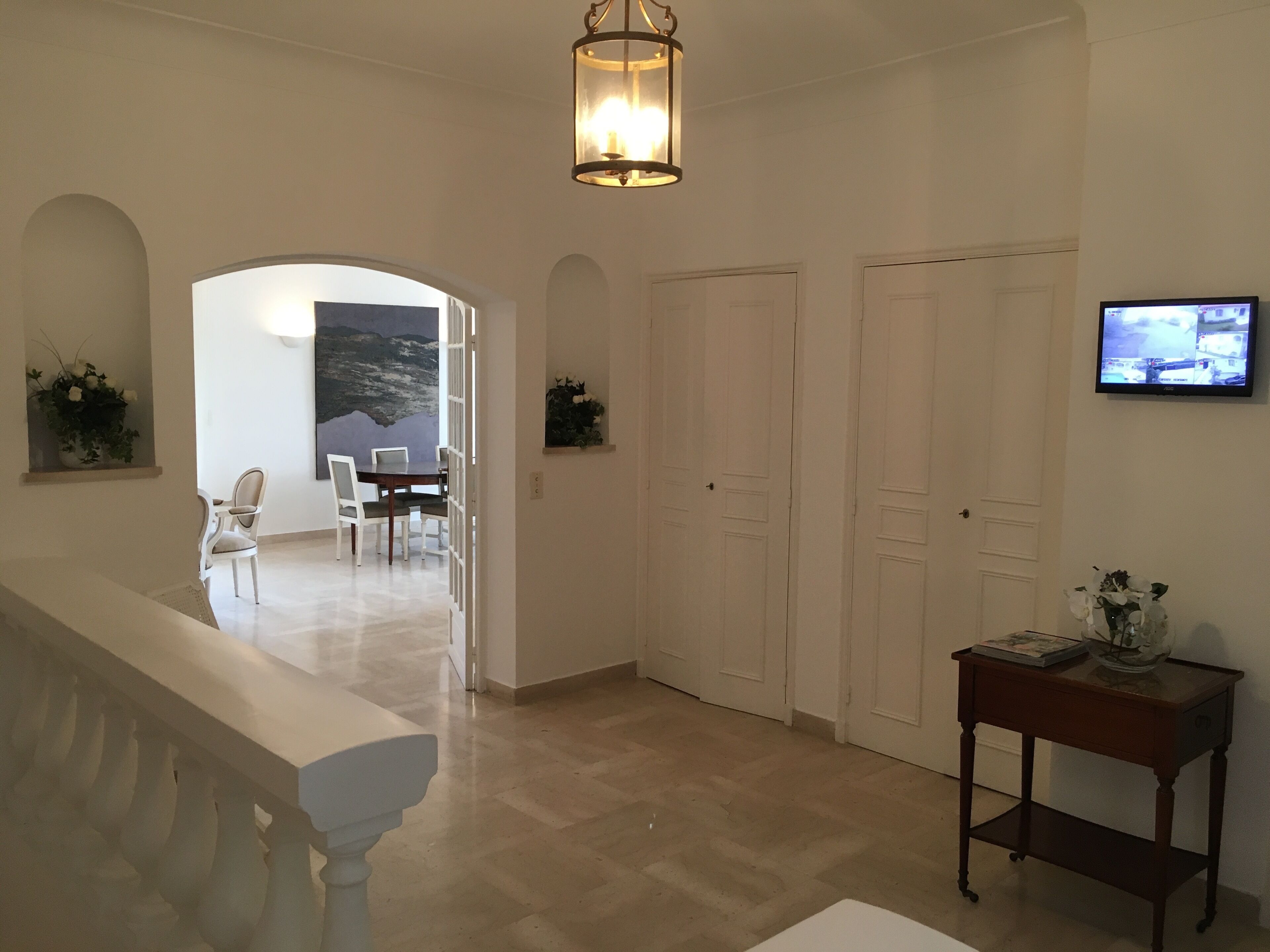 A spacious hallway with a dining area, white doors, and a television on the wall.