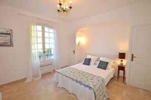 A bedroom with a large bed, a chandelier, a window with curtains, and a door. - Luxurious, gated villa with panoramic views of the Bay of Cannes, swimming pool, garden, 8 minutes from the beach (Vallauris)