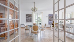 Un'ampia sala da pranzo con un tavolo rotondo e sedie, un lampadario e grandi finestre con tende.