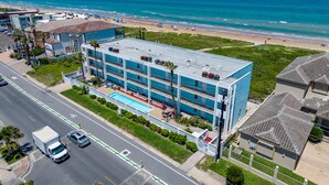 Un hotel de varios pisos con piscina en la azotea, situado cerca de una playa con vistas al océano.