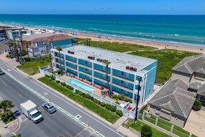 Hotel com vários andares e piscina no terraço, situado perto de uma praia com vista para o oceano.