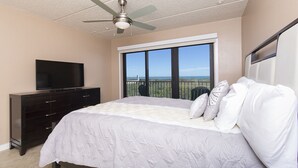 Un dormitorio con una cama grande, televisor, ventilador de techo y balcón con vistas.