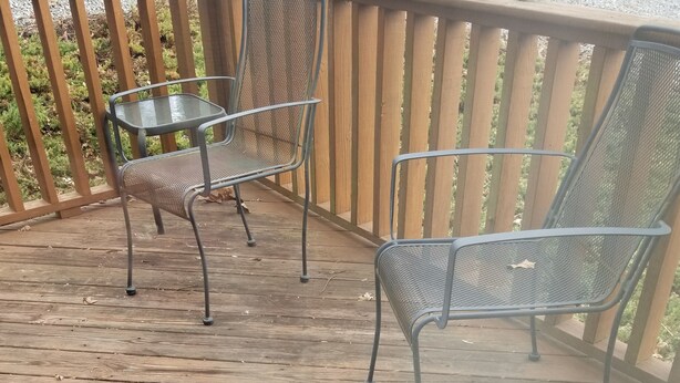 Una terraza de madera con dos sillas de metal y una mesita.
