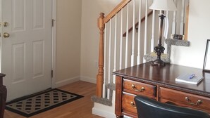 Una habitación con un escritorio de madera, una silla, una lámpara, una escalera y una puerta.