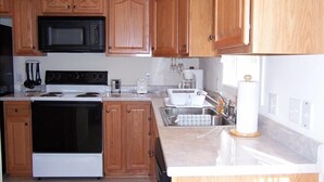 Una cocina con armarios de madera, microondas, estufa, fregadero y cafetera.