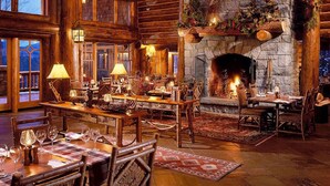 A cozy, rustic interior with wooden furniture, stone fireplace, and large windows.