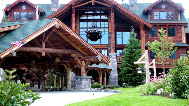 A large, rustic lodge with a prominent stone chimney, a covered porch, and a well-maintained garden.
