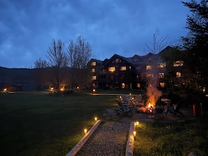 A lodge with a fire pit, outdoor seating, and a well-lit lawn area.