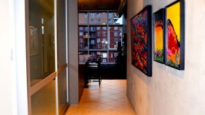 A corridor with glass doors, a tiled floor, and three artworks on the wall.