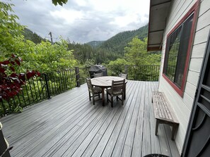 A wooden deck with a table and chairs, overlooking a forested hillside. - The Sunny Side House 4 bedroom (Alleghany)