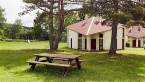 A small, single-story building with a red roof, a door, and a window. There is a picnic table in front of the building. - 2 Bedroom Cottage - Garden View (La Chapelle-Geneste)
