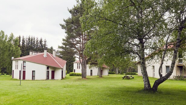 A row of white buildings with red roofs, surrounded by green grass and trees. - 2 Bedroom Cottage - Garden View (La Chapelle-Geneste)