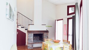 A dining area with a brick fireplace, wooden chairs, and a table with a patterned tablecloth. - 2 Bedroom Cottage - Garden View (La Chapelle-Geneste)
