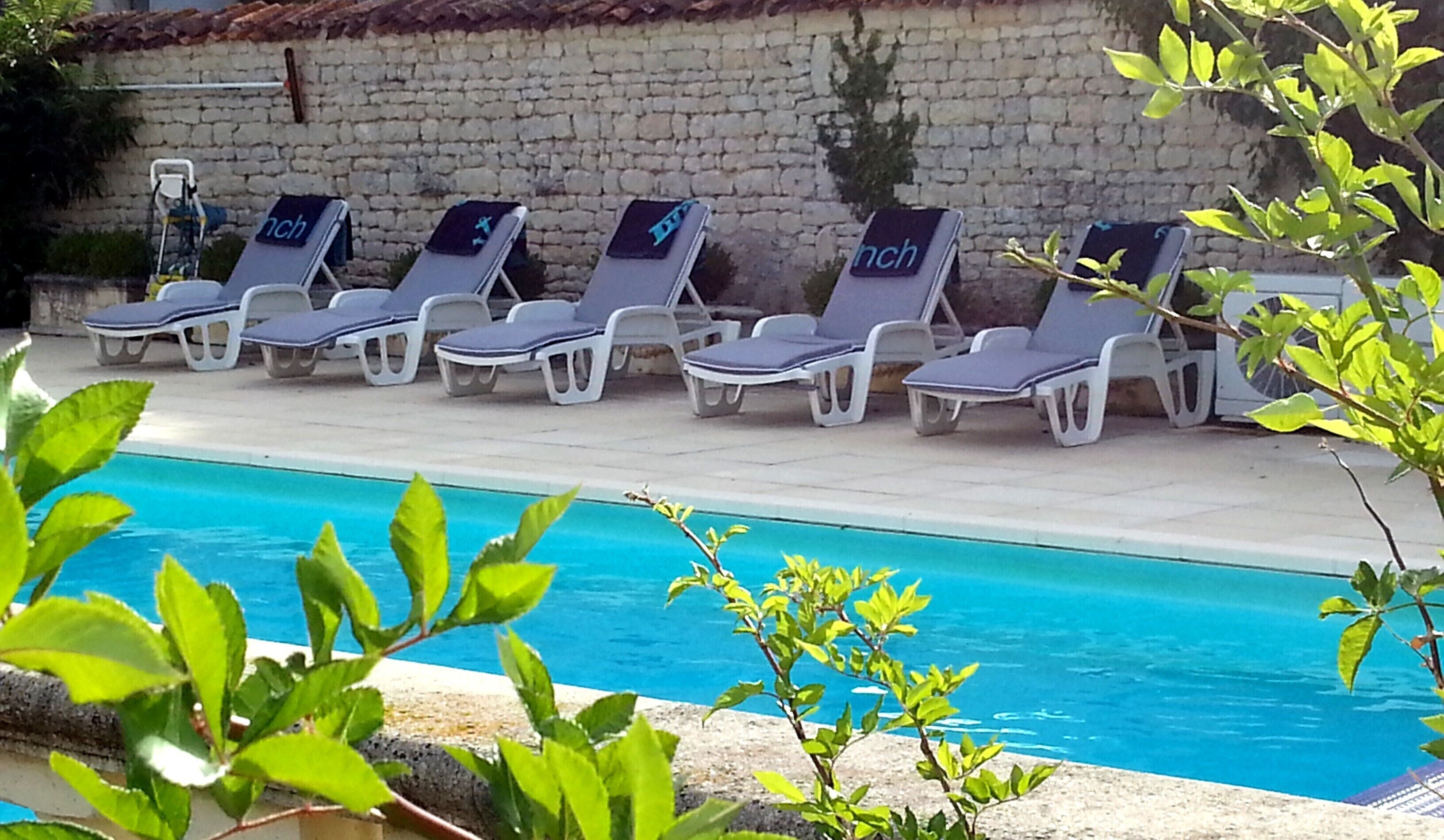 Uma área à beira da piscina com espreguiçadeiras e um muro de pedra ao fundo.