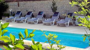 A poolside area with lounge chairs and a stone wall in the background.