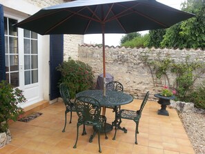 Une terrasse avec une table ronde et quatre chaises, un parasol et un mur de pierre en arrière-plan.