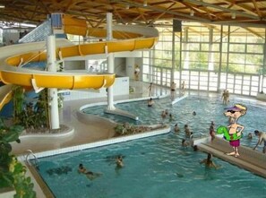 An indoor swimming pool with multiple levels and slides, surrounded by glass walls.