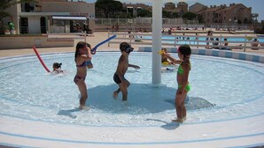 Ein Wasserspielbereich mit spielenden Kindern, ein Postamt und Gebäude im Hintergrund.