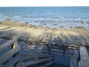 Ein hölzerner Steg führt zu einem Kiesstrand mit verstreuten Felsen.