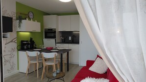 A compact kitchen with white cabinets, a dining area with two chairs, a red sofa, and a small table with two mugs. - Apartment in quiet residence facing the beach with sea view (Quiberon)