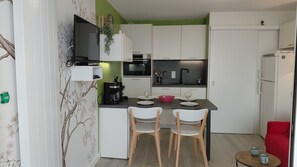 A compact kitchen with white cabinets, a black countertop, and a small dining area with two chairs. - Apartment in quiet residence facing the beach with sea view (Quiberon)